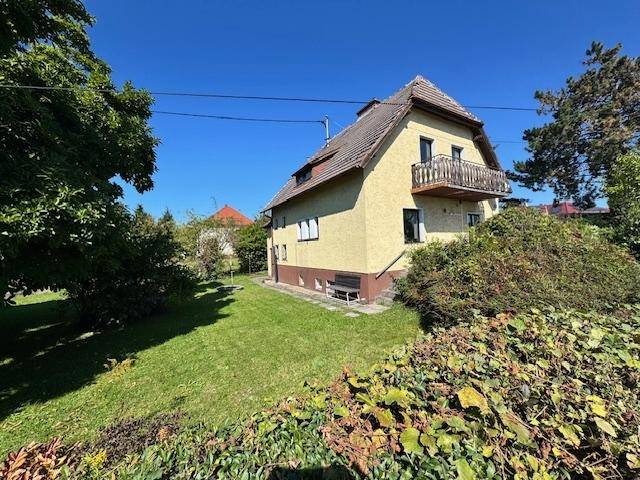 Seitenansicht des Hauses mit gepflegtem Garten, kleinem Balkon und sonnigem Himmel.