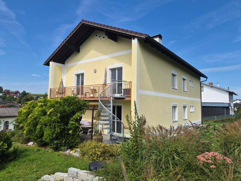 Gelbes Einfamilienhaus mit Balkon, Wendeltreppe und einer kleinen Terrasse im Gartenbereich.
