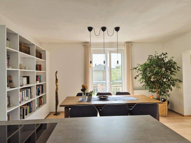 Essbereich mit großem Holztisch, Bücherregal und Blick ins Grüne durch das Fenster.