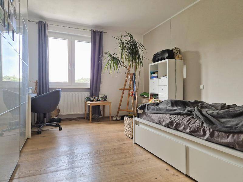 Helles Schlafzimmer mit Holzboden, großem Fenster und einem Arbeitsbereich.