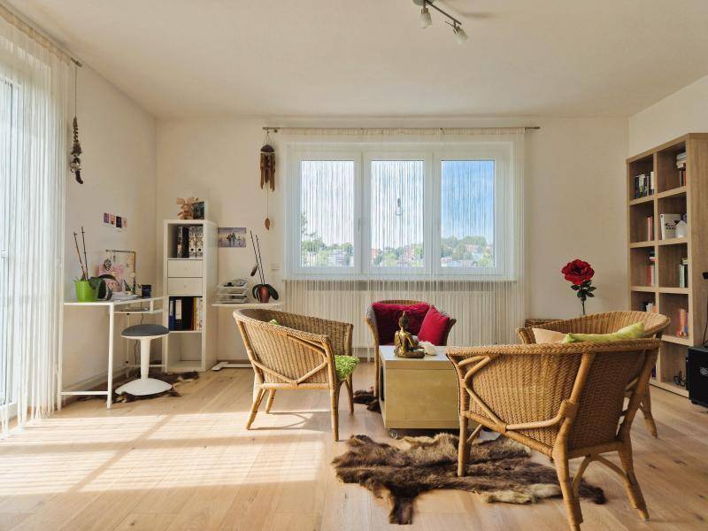 Gemütlicher Wohnbereich mit Korbsesseln, Holzboden und viel Tageslicht durch große Fenster.