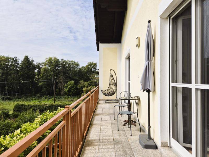 Geräumiger Balkon mit Sitzgelegenheiten, Sonnenschirm und weitem Blick ins Grüne.