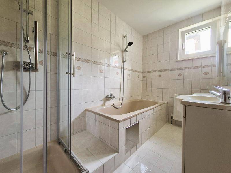 Gefliestes Badezimmer mit Badewanne, Duschkabine und Fenster für Tageslicht.