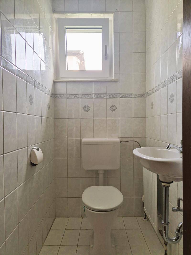 Kleines Gäste-WC mit Fenster, Toilette und Waschbecken, komplett gefliest.