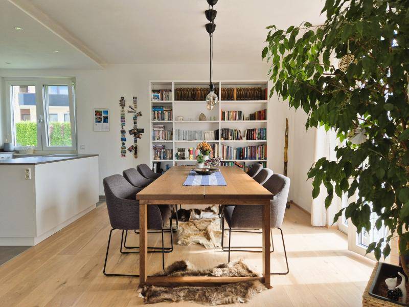 Heller Essbereich mit großem Holztisch, Bücherregal und Blick auf die moderne Küche.