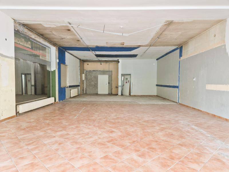 Geräumiger, leerer Geschäftsraum mit Fliesenboden, teilweise freigelegten Wänden und Deckeninstallationen.