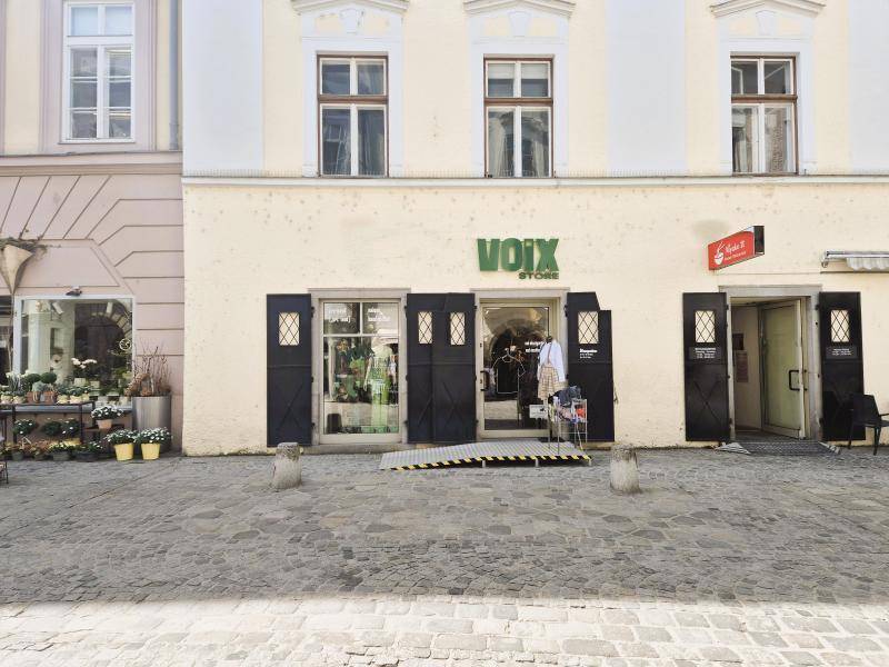 Nahaufnahme des Eingangs eines Ladenlokals mit einer Rampe und Schaufenstern in einem historischen Gebäude.