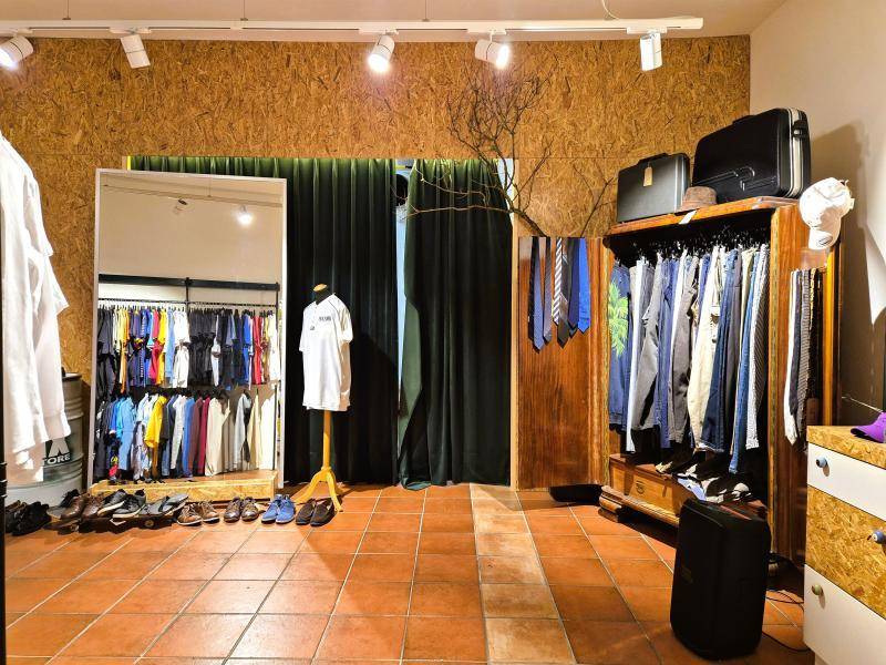 Bereich in einem Bekleidungsgeschäft mit Kleiderständern, Spiegel und Vorhängen, möglicherweise Umkleidekabinen.