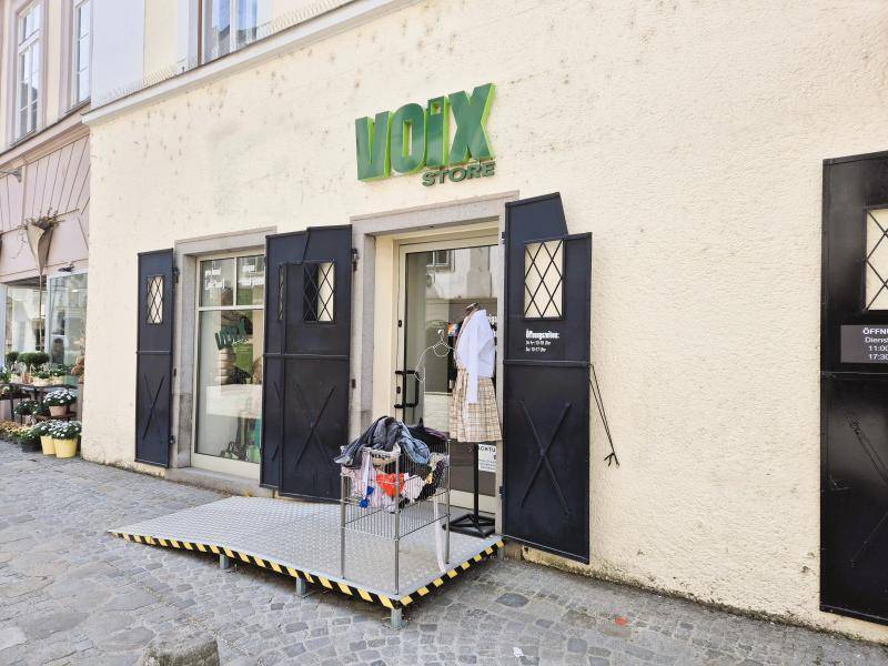 Detaillierte Ansicht des Ladeneingangs mit einer stabilen Rampe für barrierefreien Zugang und Schaufensterdekoration.