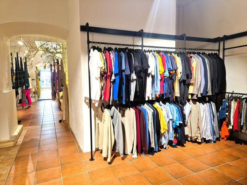 Gang in einem Bekleidungsgeschäft mit Kleiderständern voller bunter Kleidung und Terrakottafliesen.