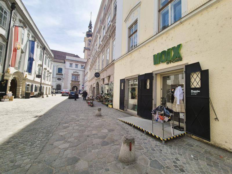 Blick entlang einer historischen Kopfsteinpflasterstraße mit Geschäften und Gebäuden unter blauem Himmel.