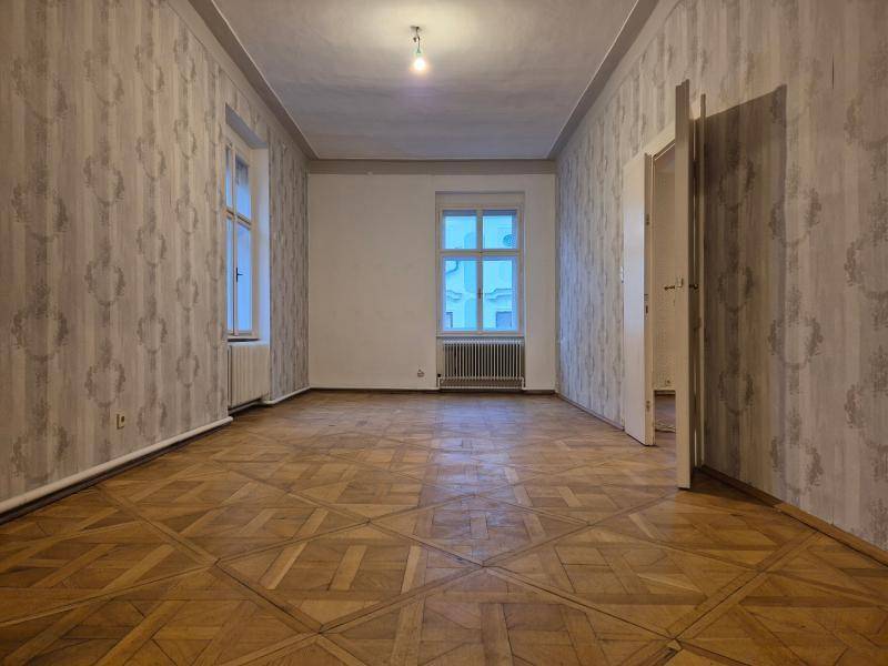 Helles, leeres Zimmer mit zwei Fenstern, die viel natürliches Licht hereinlassen, und klassischem Parkettboden.