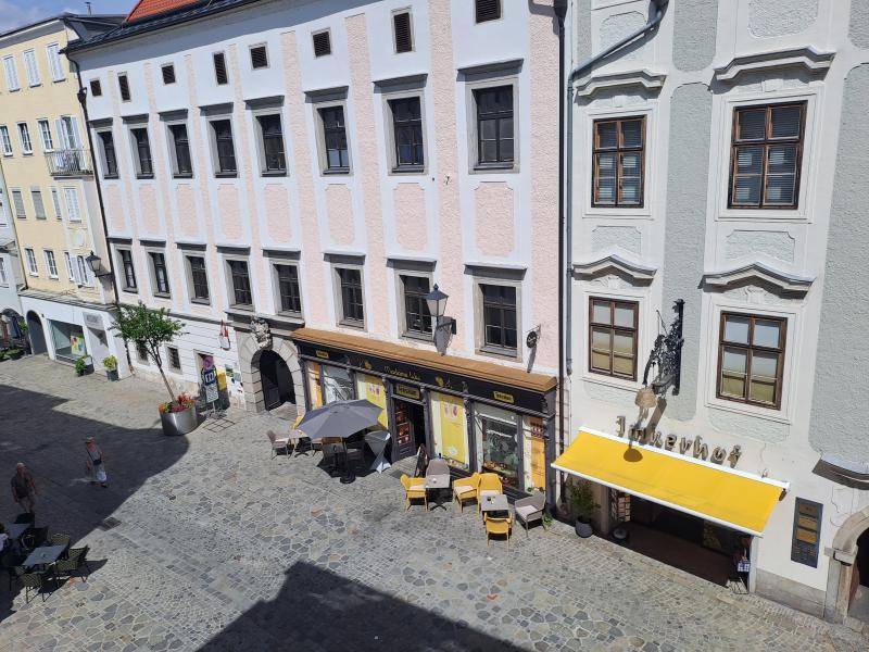 Historische Gebäudefronten an einem gepflasterten Platz mit Geschäften und Außengastronomie.