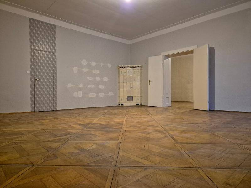 Leerer Raum mit Holzboden und einem traditionellen Kachelofen, der eine gemütliche Atmosphäre schafft.