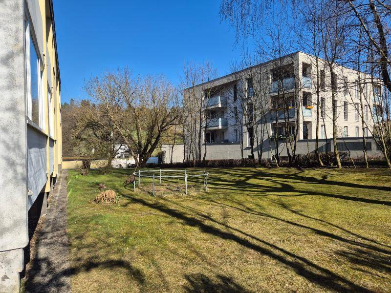 Außenansicht eines modernen Mehrfamilienhauses mit Grünfläche und Bäumen unter blauem Himmel.
