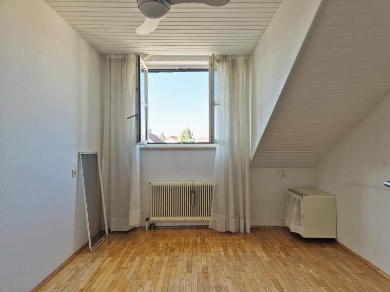 Helles Zimmer mit Parkettboden, Dachschräge und einem Fenster mit Ausblick.
