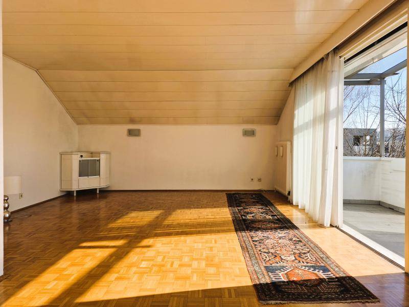 Lichtdurchflutetes Wohnzimmer mit Parkettboden, Dachschräge und Zugang zum Balkon.