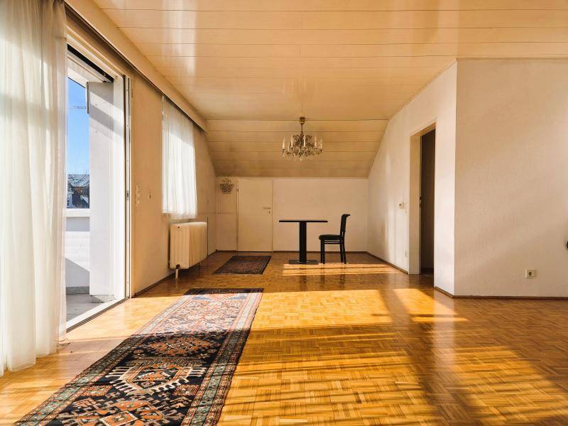 Helles Wohnzimmer mit Parkettboden, Dachschräge und Zugang zu einem sonnigen Balkon.