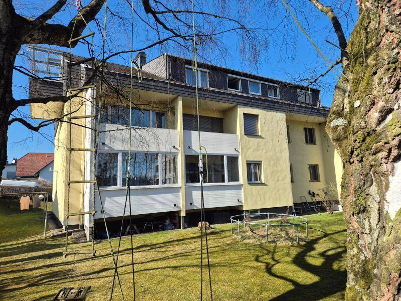 Mehrfamilienhaus mit gelber Fassade, Balkonen und einem großen Gartenbereich.