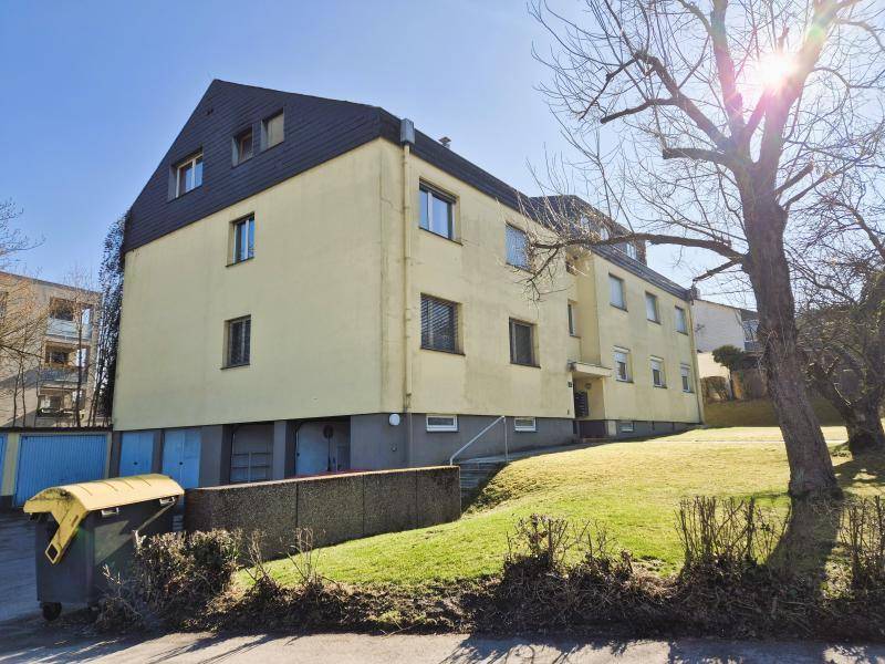 Rückansicht eines Mehrfamilienhauses mit gelber Fassade und Garagen im Untergeschoss.