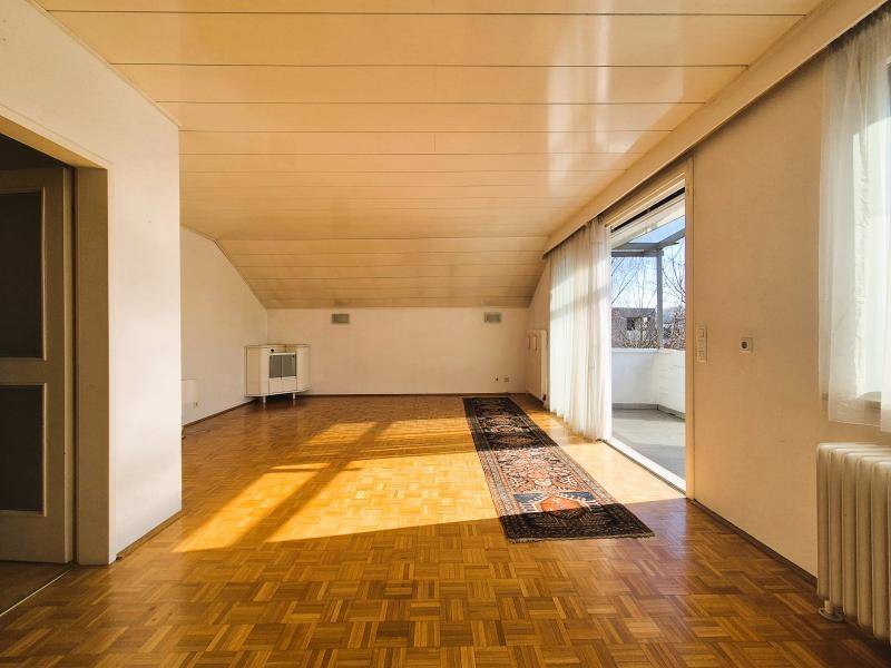 Geräumiges Wohnzimmer mit Parkettboden, Dachschräge und breitem Zugang zum Balkon.