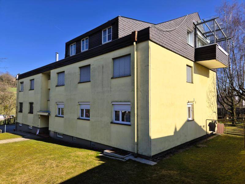 Seitenansicht des Gebäudes mit gelber Fassade, Dachschräge und einem verglasten Balkon.