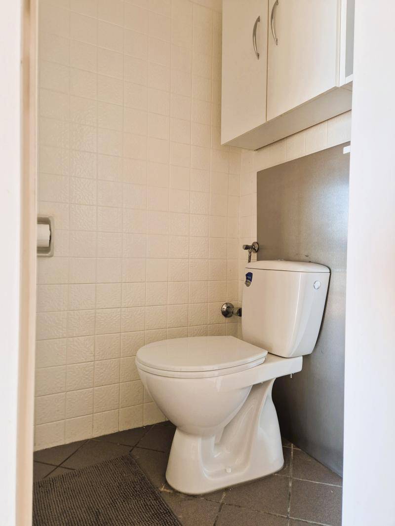 Kleines WC mit hellen Fliesen und wandmontierten Schränken über der Toilette.