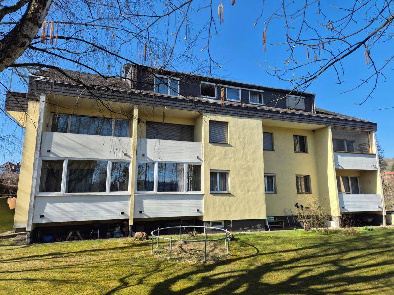 Mehrfamilienhaus mit gelber Fassade, Balkonen und einem gepflegten Rasenbereich.