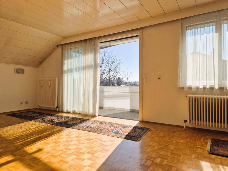 Helles Wohnzimmer mit Parkettboden, Dachschräge und Zugang zu einem Balkon.