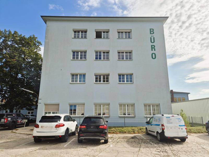 Ansicht eines mehrstöckigen Bürogebäudes mit vielen Fenstern und einem Parkplatz davor.