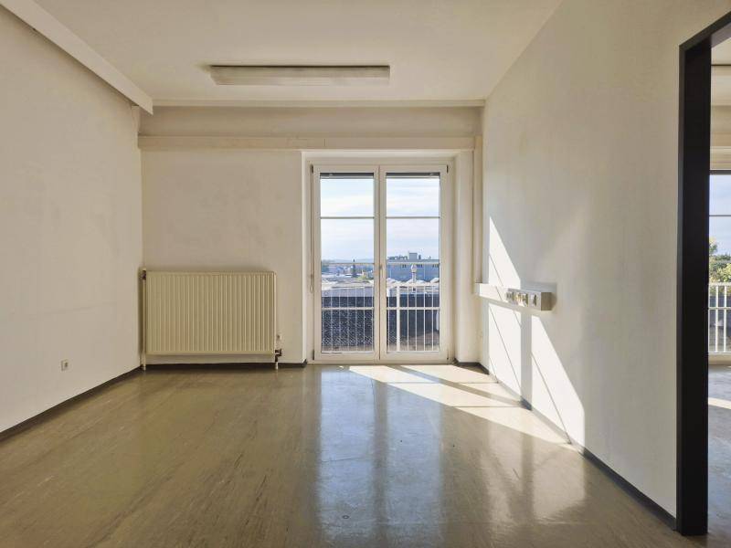Heller Büroraum mit großen Fenstern und Zugang zu einem Balkon, der viel Sonnenlicht bietet.