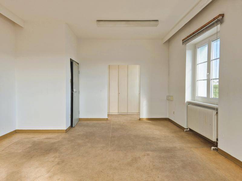 Leerer Büroraum mit einfacher Ausstattung, einem Fenster und einem Einbauschrank im Hintergrund.