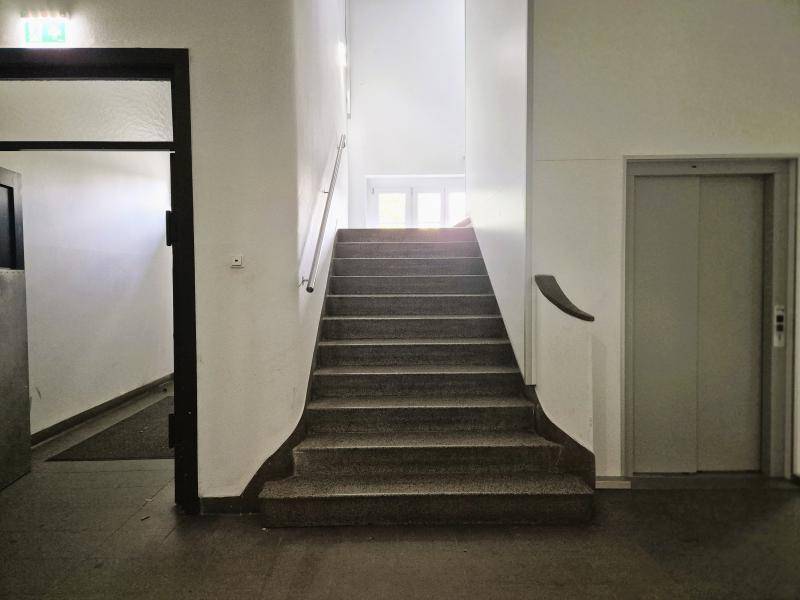 Treppenhaus mit Steinstufen und Handlauf, daneben ein Aufzug, der die Etagen verbindet.