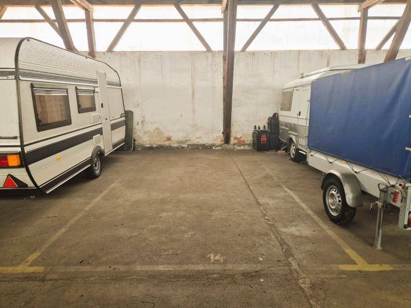 Stellplatz Nummer 14 in der Lagerhalle mit einem Wohnwagen und einem Anhänger unter Holzdachkonstruktion.