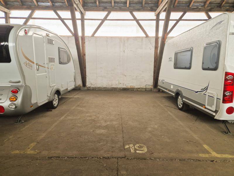 Innenansicht einer Lagerhalle mit zwei geparkten Wohnwagen und markiertem Stellplatz auf Betonboden.