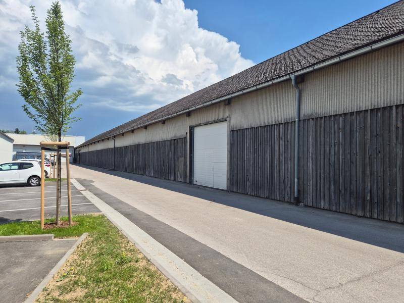 Lange Lagerhalle mit dunkler Holzfassade, Wellblechdach und großem Garagentor unter blauem Himmel.