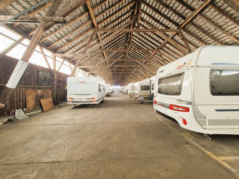 Weitläufige Lagerhalle mit zahlreichen geparkten Wohnwagen und beeindruckender Holzdachkonstruktion.