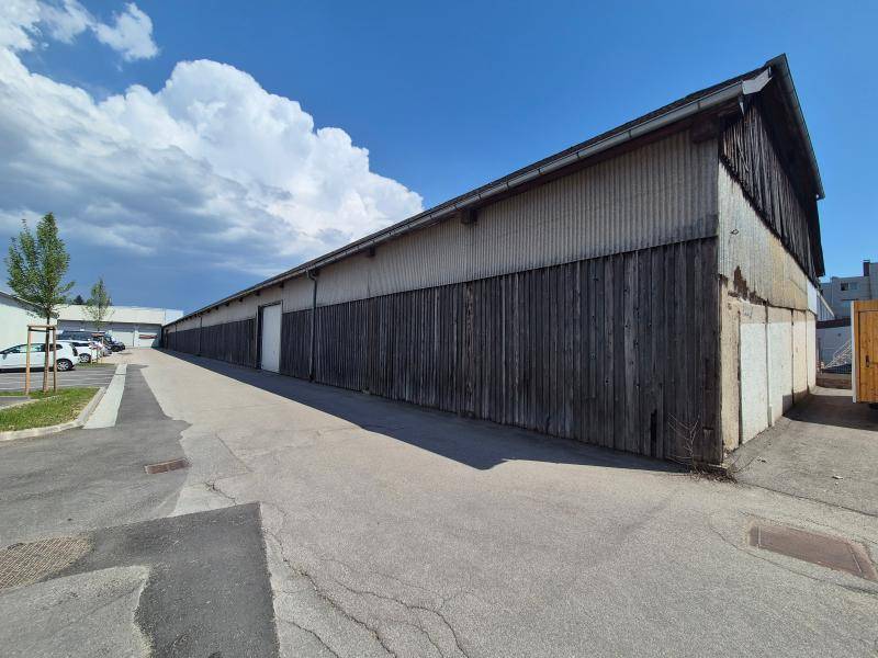 Außenansicht der langen Lagerhalle mit Holzfassade, Wellblechdach und angrenzenden Parkplätzen.