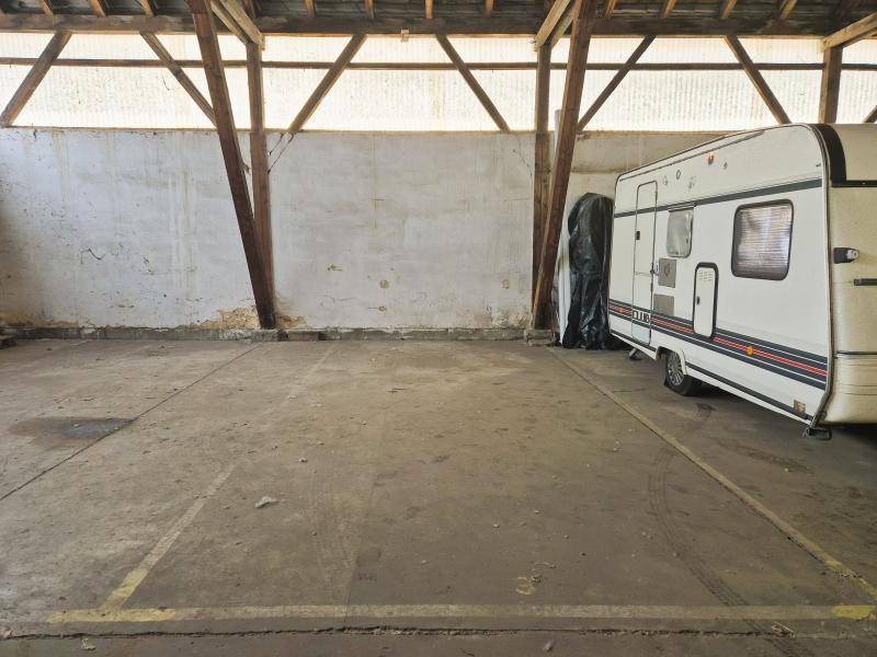 Leerer Stellplatz in der Lagerhalle neben einem Wohnwagen, mit sichtbarer Holzbalkenkonstruktion und Betonboden.