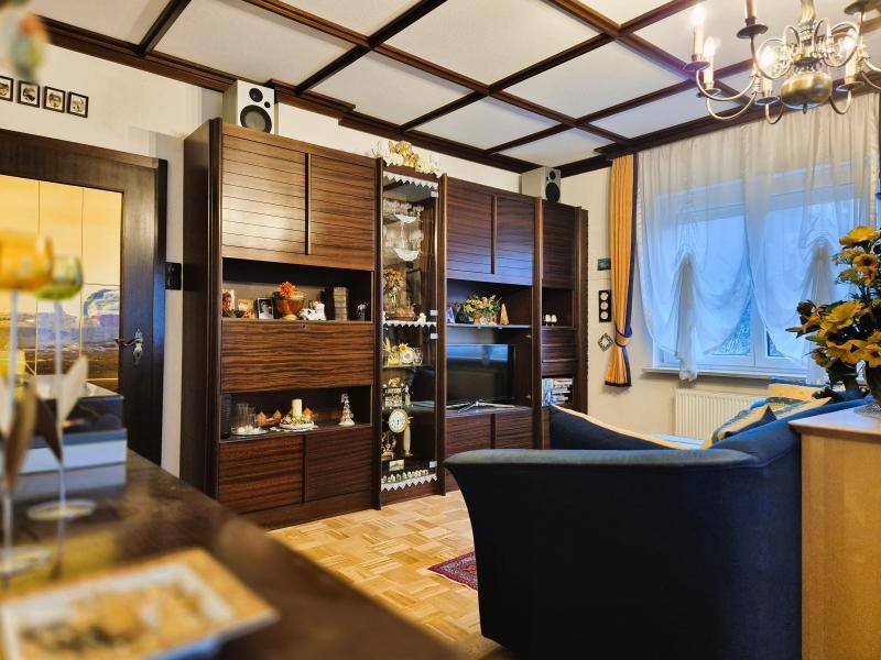 Wohnzimmer mit großer dunkler Holzschrankwand, Holzbalkendecke und traditioneller Einrichtung.