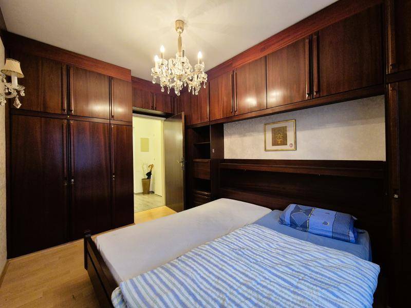 Schlafzimmer mit Doppelbett und umfangreichen dunklen Einbauschränken, beleuchtet von Kronleuchter.