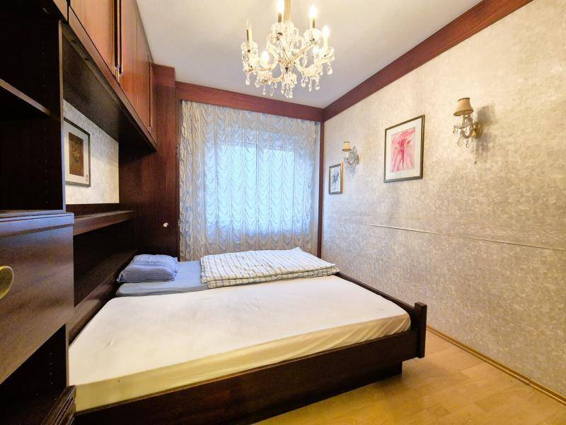 Schlafzimmer mit Einzelbett, dunklen Einbaumöbeln und Kronleuchter, hell tapeziert.