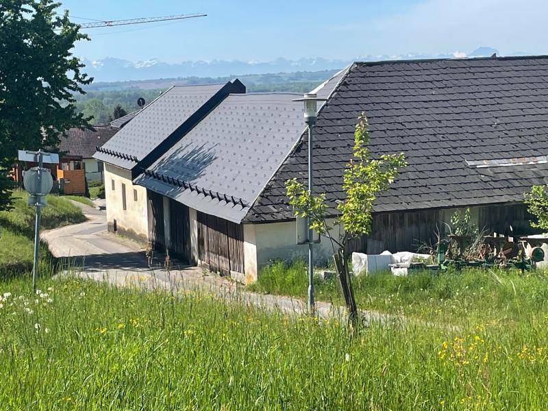 Ländliche Gebäude mit dunklen Dächern und weitem Blick auf die Alpenkette im Hintergrund.
