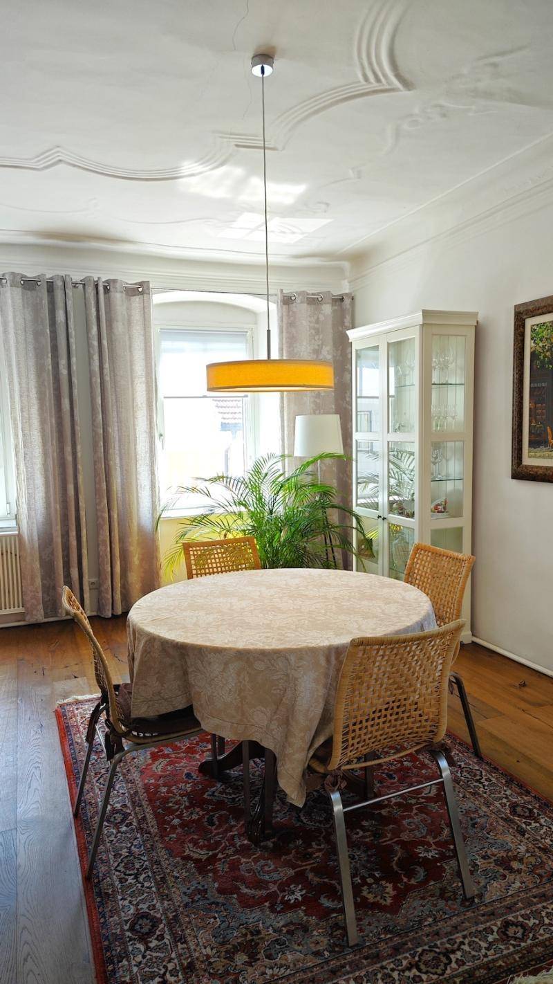 Gemütlicher Essbereich mit rundem Tisch, Korbstühlen und einem Fenster mit Vorhängen.