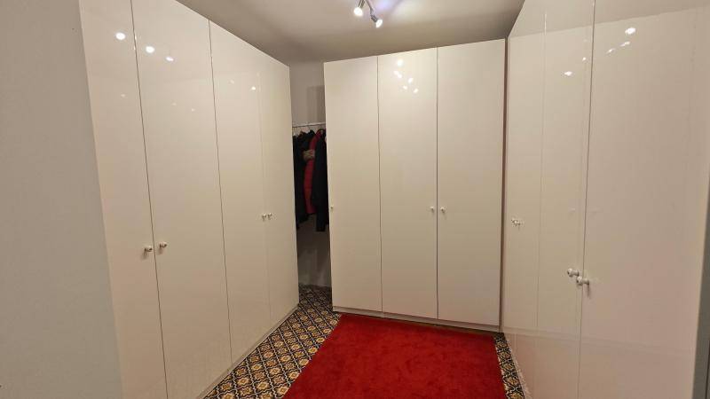 Begehbarer Kleiderschrank mit vielen weißen Hochglanzschränken und gemustertem Boden.