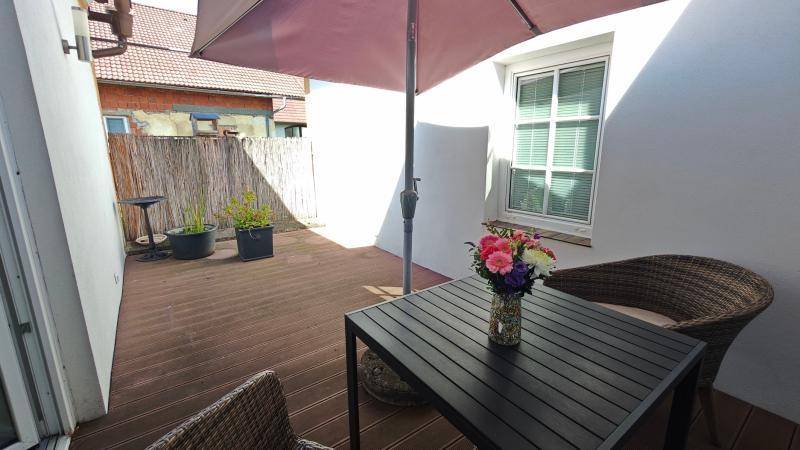 Sonniger Terrassenbereich mit Holzboden, Gartenmöbeln und einem großen Sonnenschirm.