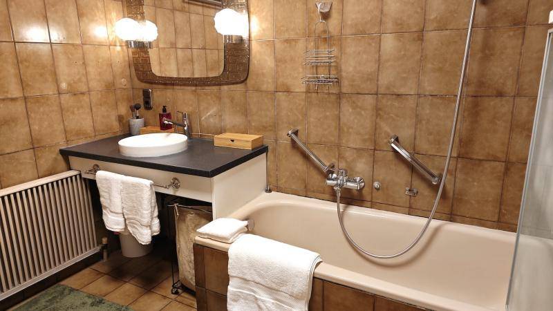 Badezimmer im 80er-Jahre-Stil mit braunen Fliesen, Badewanne und Waschtisch.