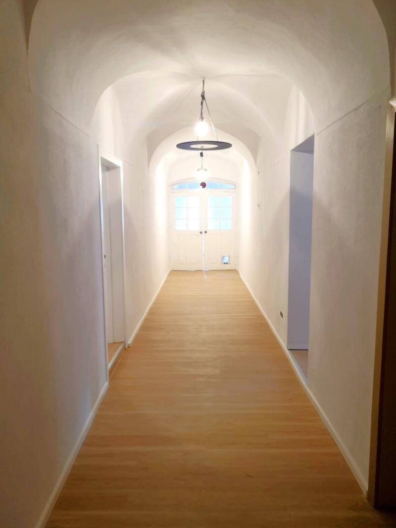 Langer, heller Flur mit Gewölbedecke, Holzboden und einer Doppeltür am Ende.