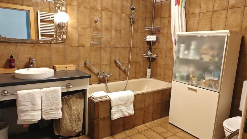 Badezimmer mit braunen Fliesen, Badewanne, Waschtisch und einem Spiegelschrank.