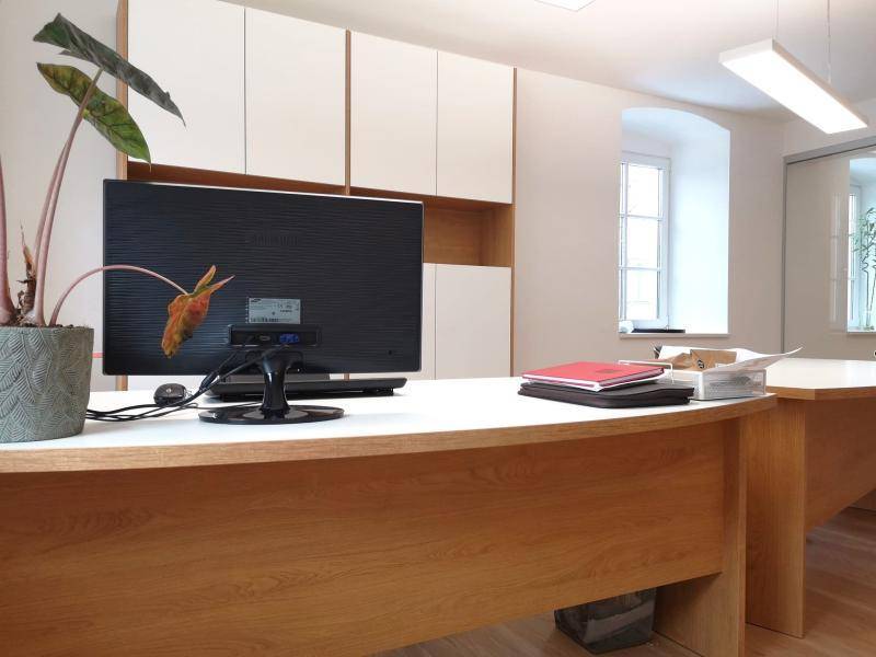 Heller Büroraum mit modernen Holzschreibtischen, weißen Schränken und großen Fenstern.